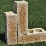 Three Sunrise Travertine face bricks displayed outdoors on grass in an L-shape arrangement showing pitted travertine surface texture, core holes, and warm apricot-tan tones.