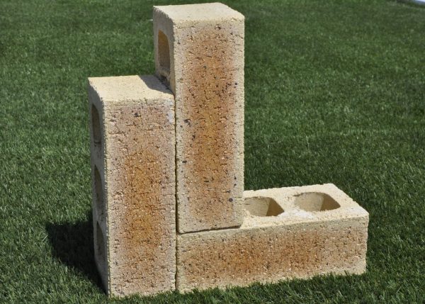 Three Sunrise Travertine face bricks displayed outdoors on grass in an L-shape arrangement showing pitted travertine surface texture, core holes, and warm apricot-tan tones.