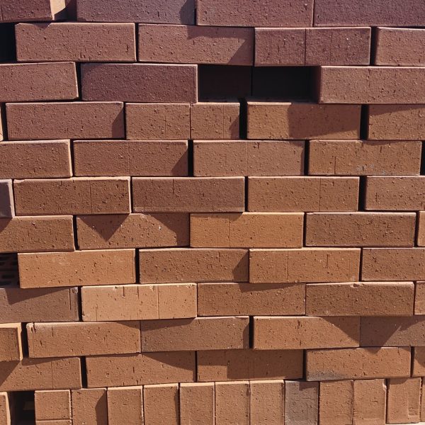 Front-on view of stacked FBA Terracotta Travertine non-standard face bricks showing pitted travertine texture, rustic terracotta-red to burnt-orange body tone variations, and fine iron speckling.