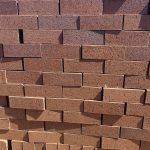 Front-on view of stacked FBA Terracotta Travertine non-standard face bricks showing pitted travertine texture, rustic terracotta-red to burnt-orange body tone variations, and fine iron speckling.