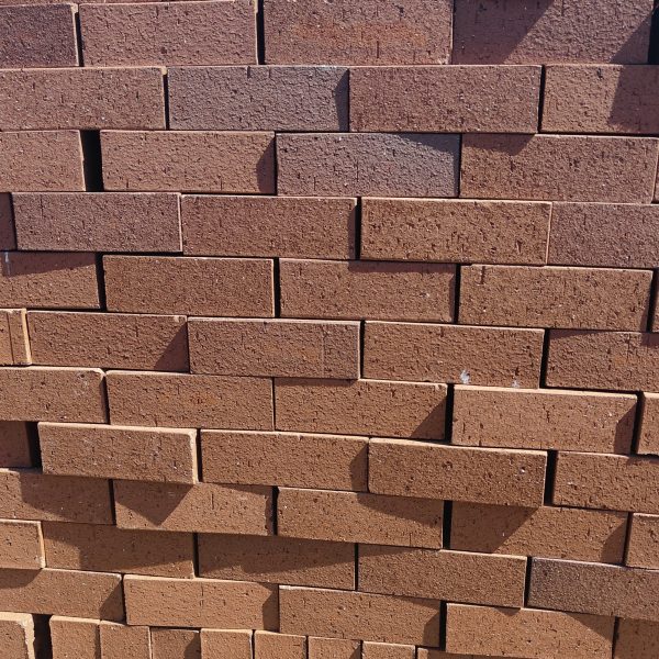 Front-on view of stacked FBA Terracotta Travertine non-standard face bricks showing pitted travertine texture, rustic terracotta-red to burnt-orange body tone variations, and fine iron speckling.