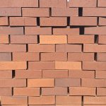 Front-on view of stacked Terracotta Travertine Flash face bricks showing pitted travertine texture, multi-toned warm red and peach clay body, and subtle dark heat-flashed reduction variations.