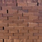 Front-on view of stacked FBA Terracotta Travertine face bricks showing pitted travertine texture, deep terracotta-red clay body, and subtle dark heat-flashing highlights under direct sunlight.