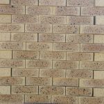 Front-on view of stacked Topaz Travertine face bricks showing pitted travertine surface texture, light golden-buff clay body, warm tan heat-flashed reduction centers, and heavy dark iron speckling.