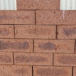 Outdoor pyramid stack arrangement of Wild Wheat Travertine face bricks showing pitted travertine surface texture, earthy red-brown clay body, and dark charcoal heat-flashed centers.